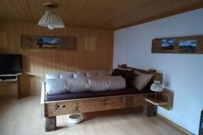 Un lit en bois avec des oreillers, une table de chevet, une lampe et un téléviseur posé sur un meuble.