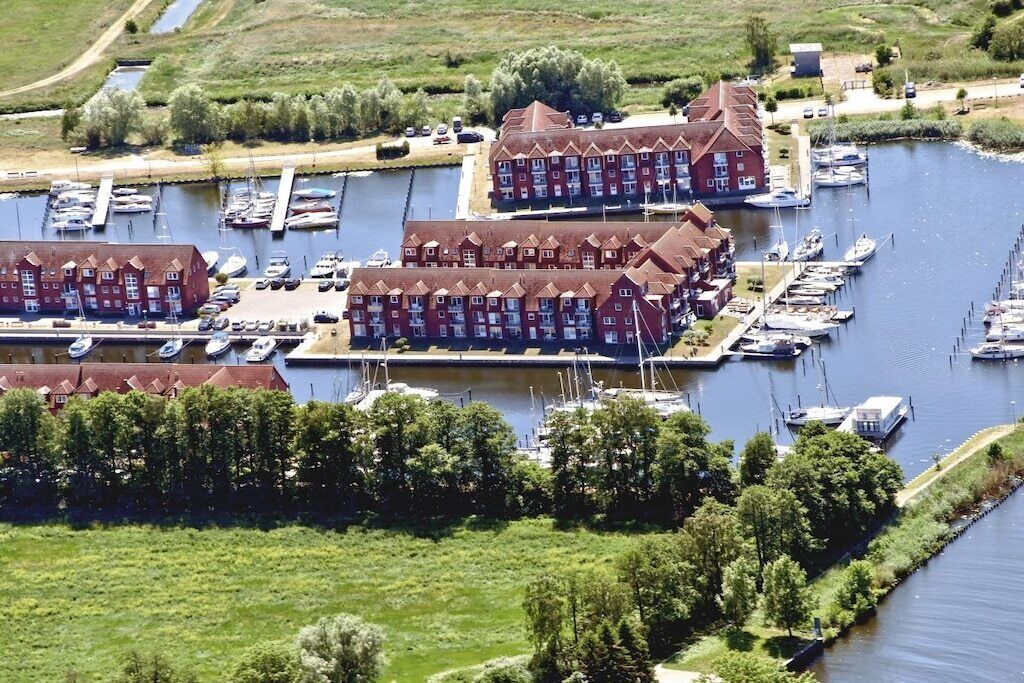 A marina with multiple boats docked, a red building with a gabled roof, and a grassy area with trees.