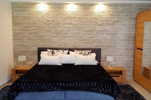 A bedroom with a stone-patterned wall, a bed with a black cover, two bedside tables with lamps, and a wooden wardrobe. - Apartment in Ueckermünde with swimming pool (Ueckermünde)