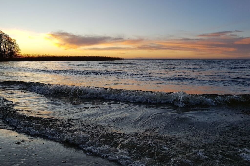 A coastal landscape with a body of water, waves, and a distant shoreline.