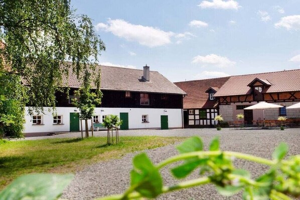 A building with a tiled roof and a white facade, a gravel courtyard, and a tree. - Holiday apartment in Redwitz with sauna (Redwitz)