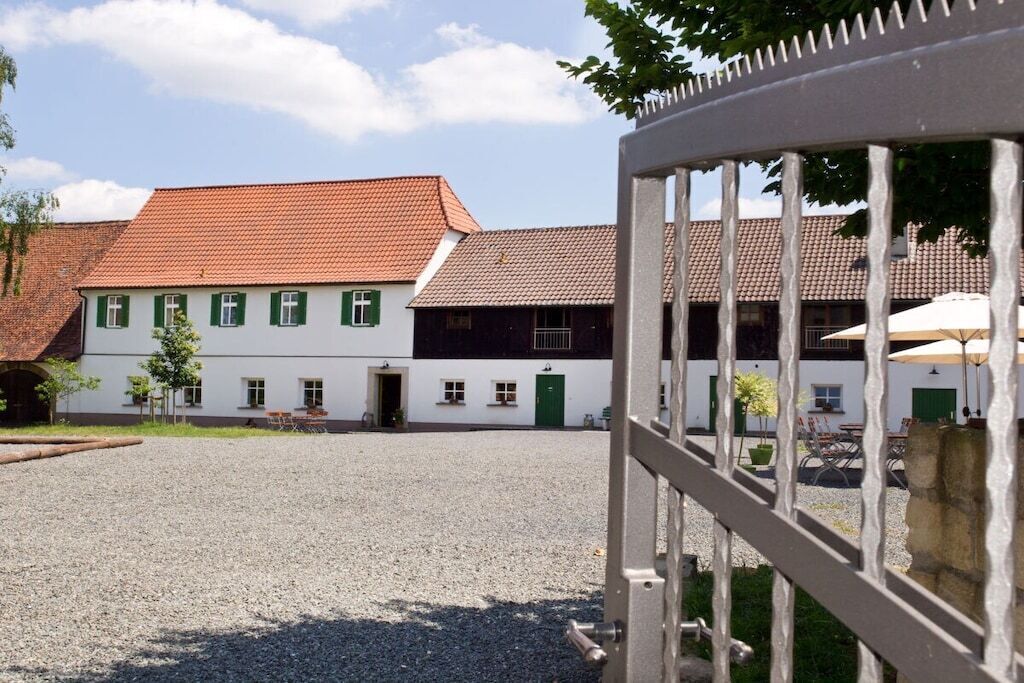 A building with a gravel courtyard, a white facade with green shutters, and a red-tiled roof.