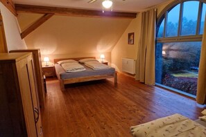 A bedroom with a wooden floor, a bed with pillows, a nightstand with a lamp, and a window with curtains. - Holiday apartment in Redwitz with sauna (Redwitz)