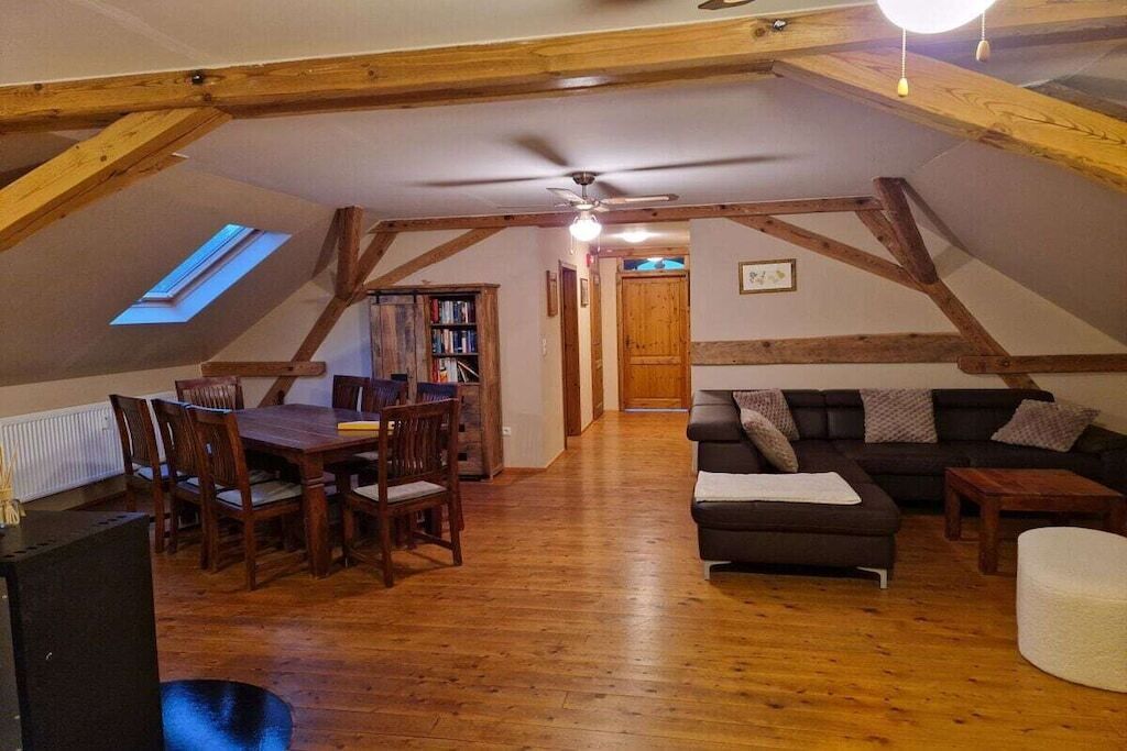 A loft-style room with a dining table, chairs, a sofa, and a ceiling fan.