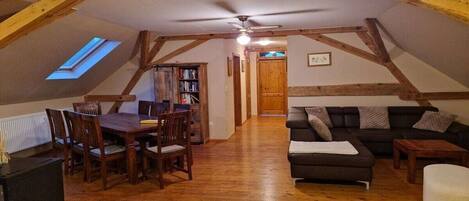 A loft-style room with a dining table, chairs, a sofa, and a ceiling fan.