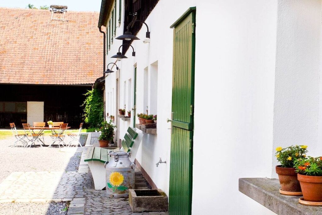 Un patio con una mesa y sillas, plantas en macetas y un edificio con una puerta verde.