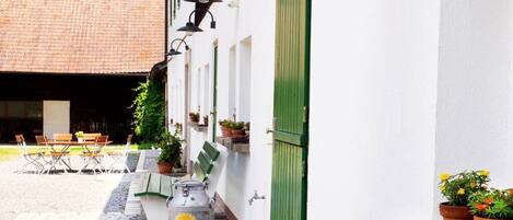 Un patio con una mesa y sillas, plantas en macetas y un edificio con una puerta verde.
