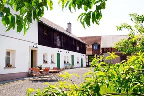 A building with a white facade and a dark wooden section, featuring a gravel courtyard with outdoor seating. - Holiday apartment in Redwitz with sauna (Redwitz)