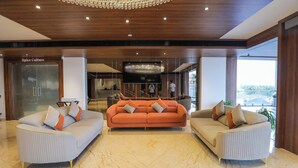 Un hall d’entrée moderne avec un grand canapé orange, deux canapés blancs, un lustre et un grand téléviseur à écran plat.