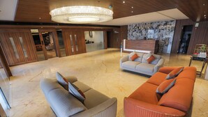 A spacious lobby with a marble floor, a large chandelier, and seating arrangements including sofas and armchairs.