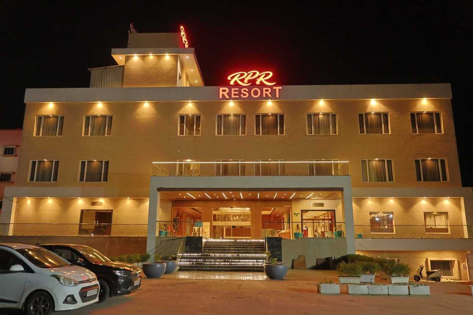Un hotel con un llamativo letrero de neón, una entrada imponente y un estacionamiento con coches.