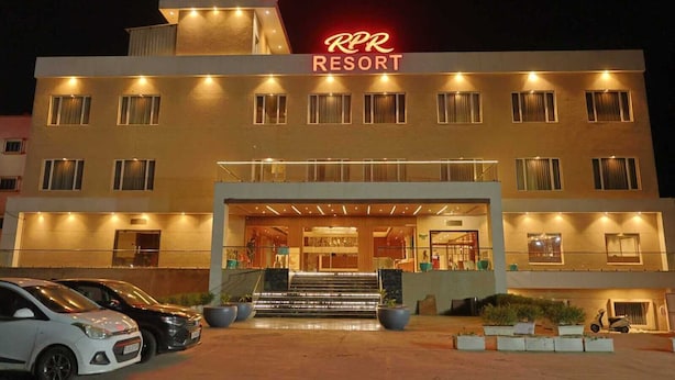 Un hôtel reconnaissable à son grand panneau lumineux, à son entrée imposante et à son parking rempli de voitures.