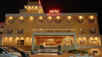 Un hotel con un llamativo letrero de neón, una entrada imponente y un estacionamiento con coches.