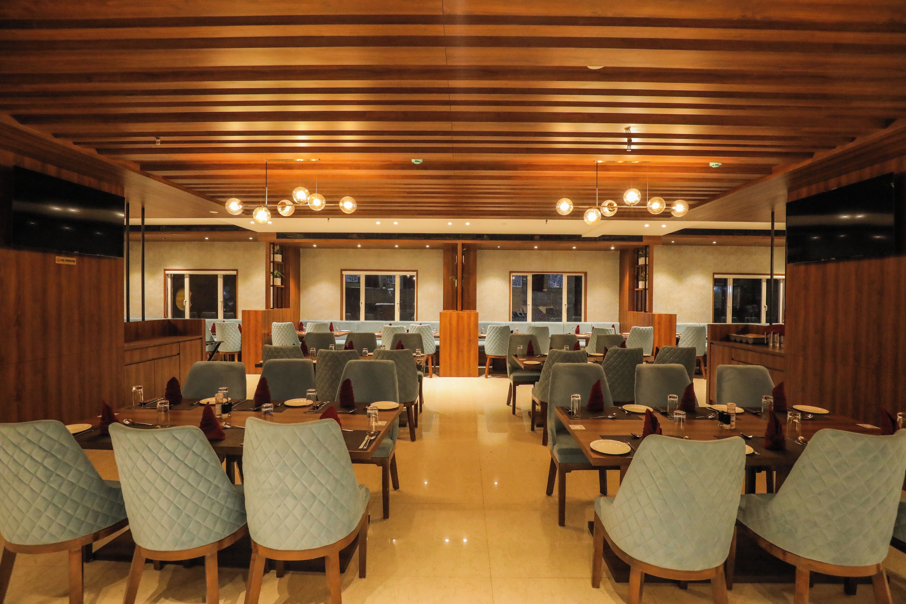 Un comedor de hotel con varias mesas y sillas, paneles de madera en las paredes e iluminación empotrada en el techo.