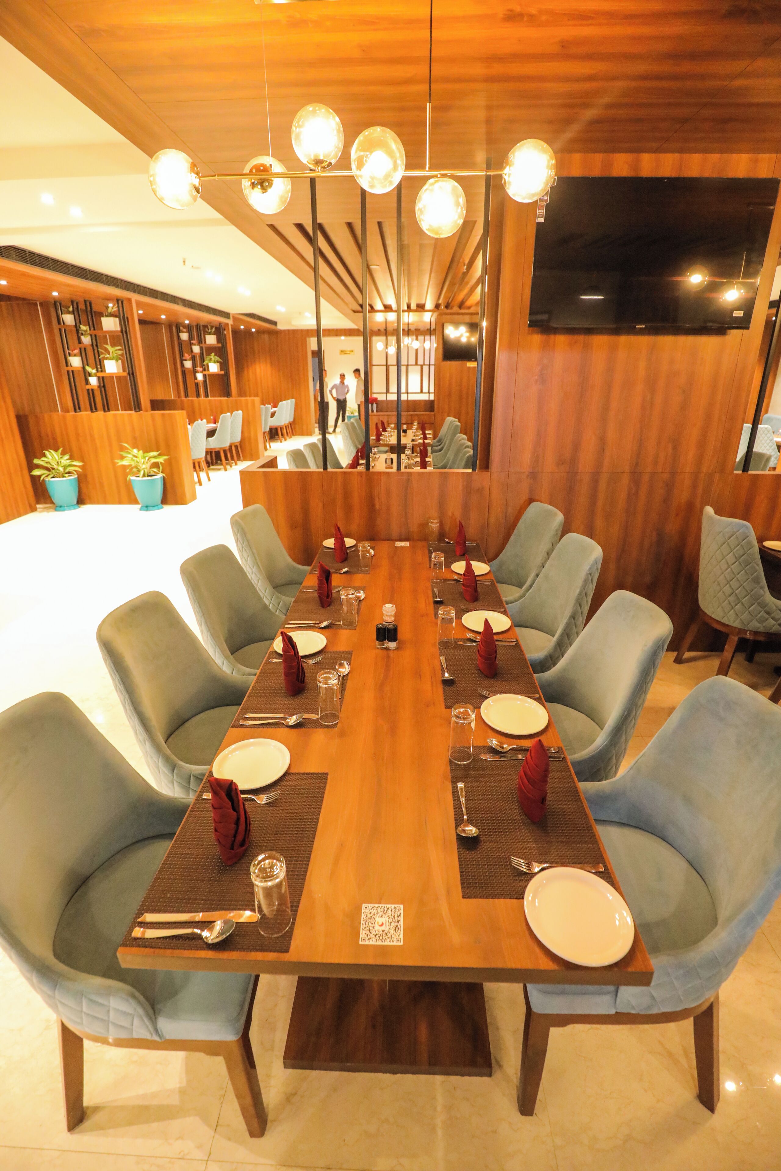 A dining area with a long wooden table set for six, surrounded by upholstered chairs.