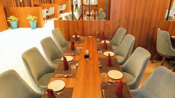 A dining area with a long wooden table set for six, surrounded by upholstered chairs.