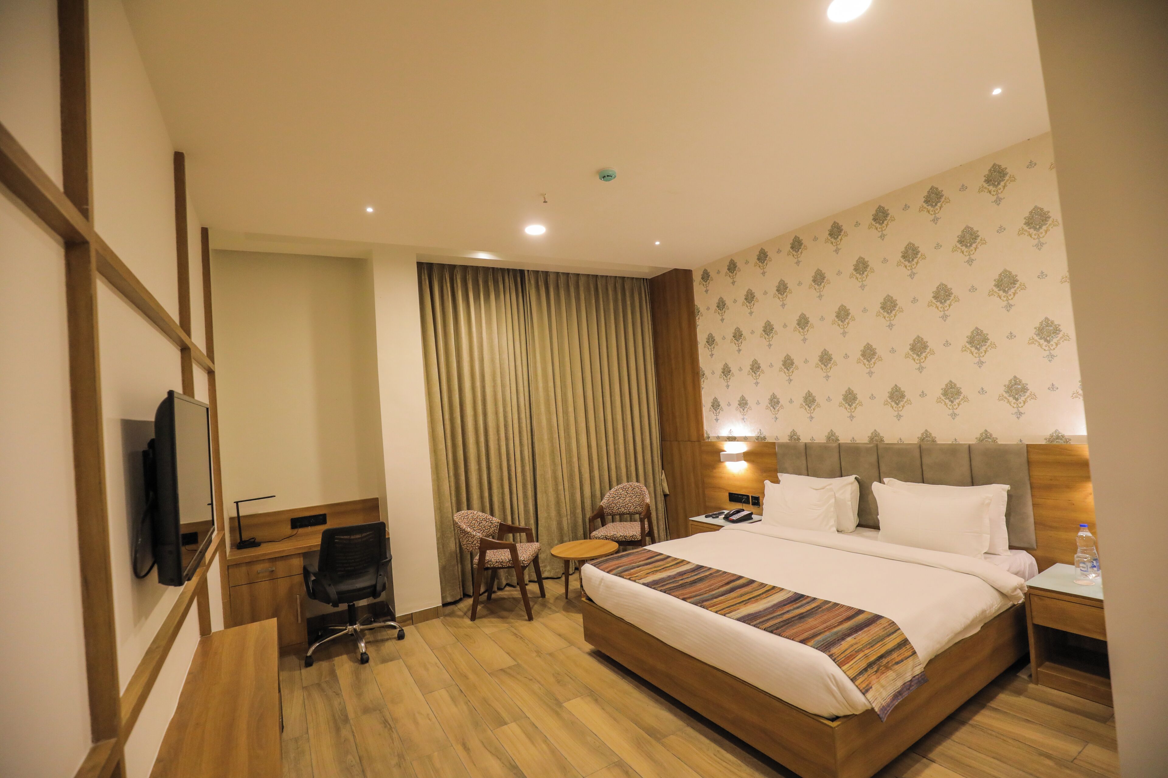 Quarto de hotel com uma cama grande, uma escrivaninha com cadeira, uma mesinha e uma televisão.