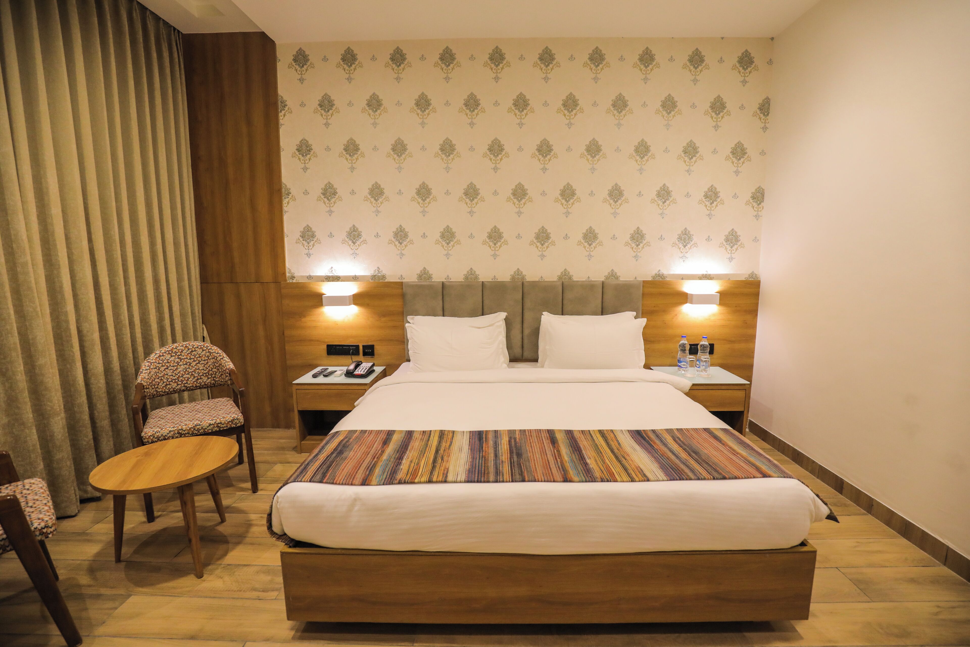 Una habitación de hotel con una cama grande, dos mesitas de noche, una silla y un cabecero de madera.