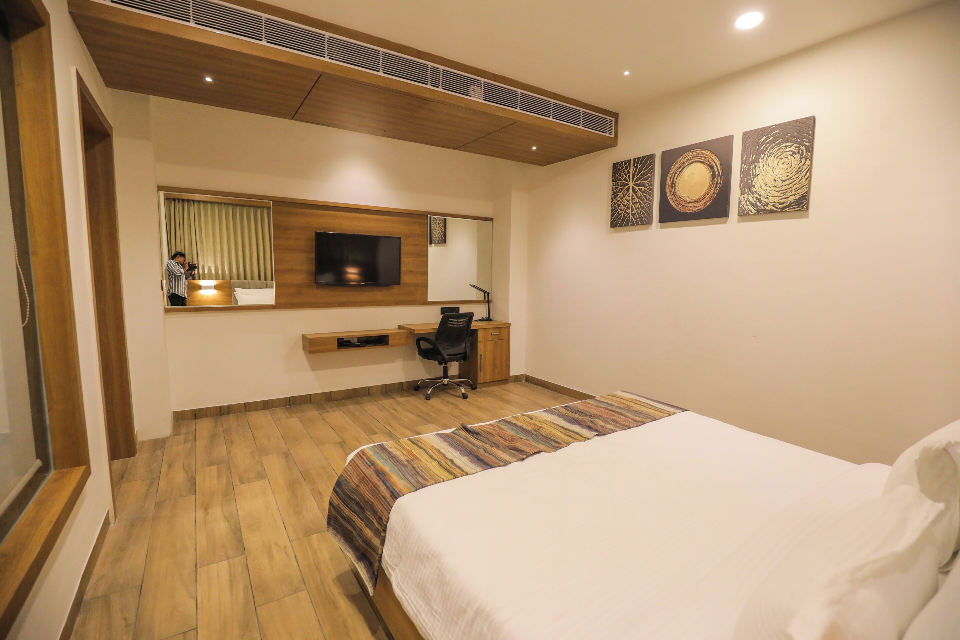 Ein Hotelzimmer mit Bett, Schreibtisch, Stuhl, Fernseher und Bildern an der Wand.