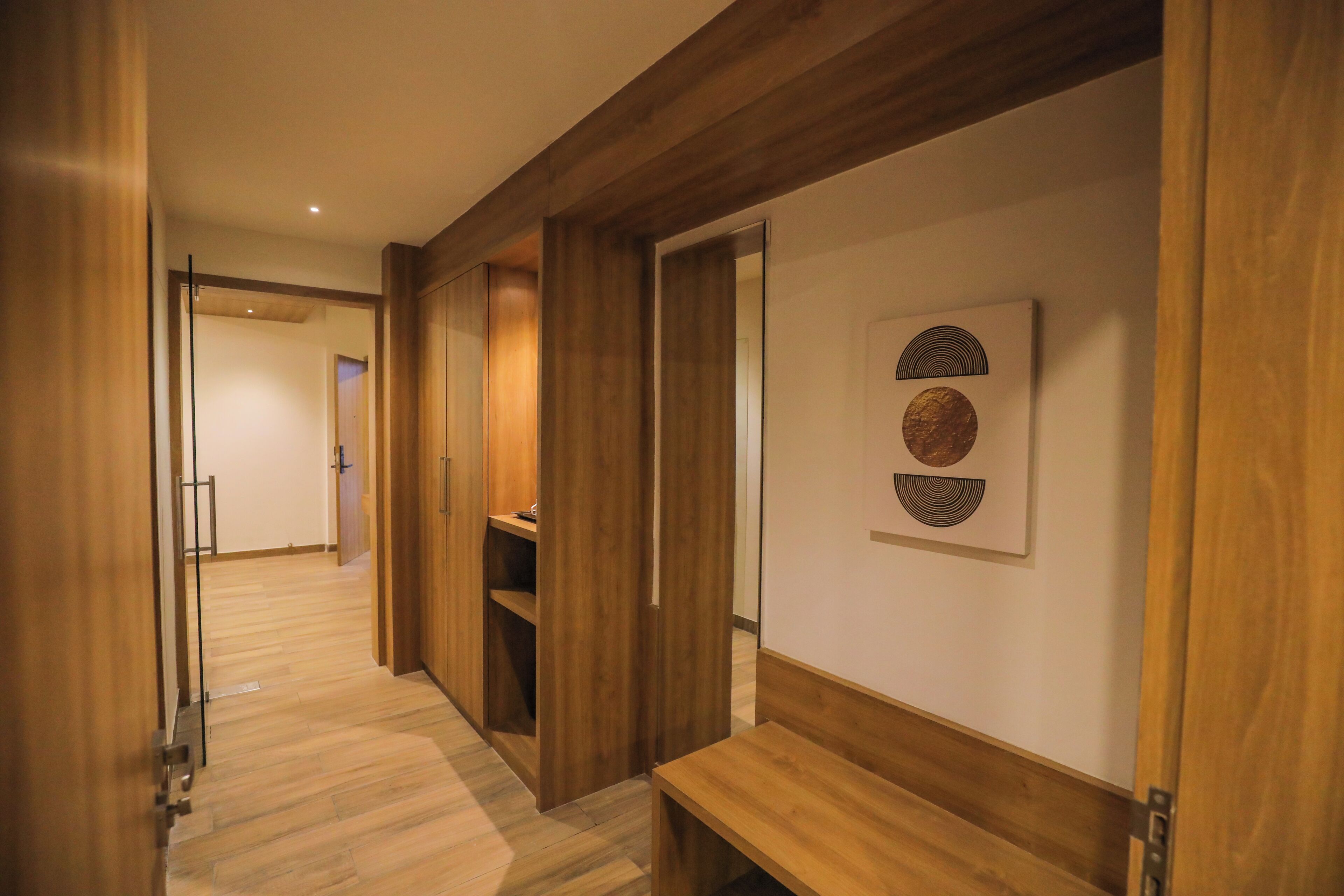 Un pasillo con suelo de madera y paredes, un banco y una puerta que da a otra habitación.