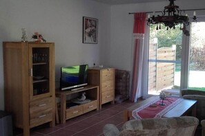 Ein Wohnzimmer mit Fernseher, Holzschrank und einem fenster mit Vorhängen.