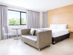 Habitación de hotel con cama, sofá, sillón, una mesita y ventana con cortinas.