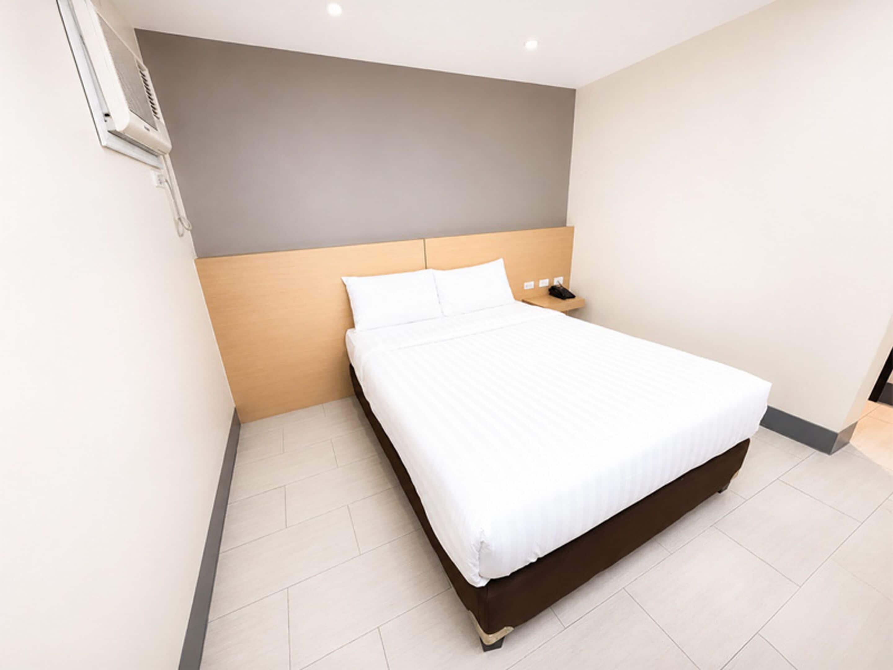 Quarto de hotel moderno com uma cama grande, mesa de cabeceira e ar condicionado de parede.