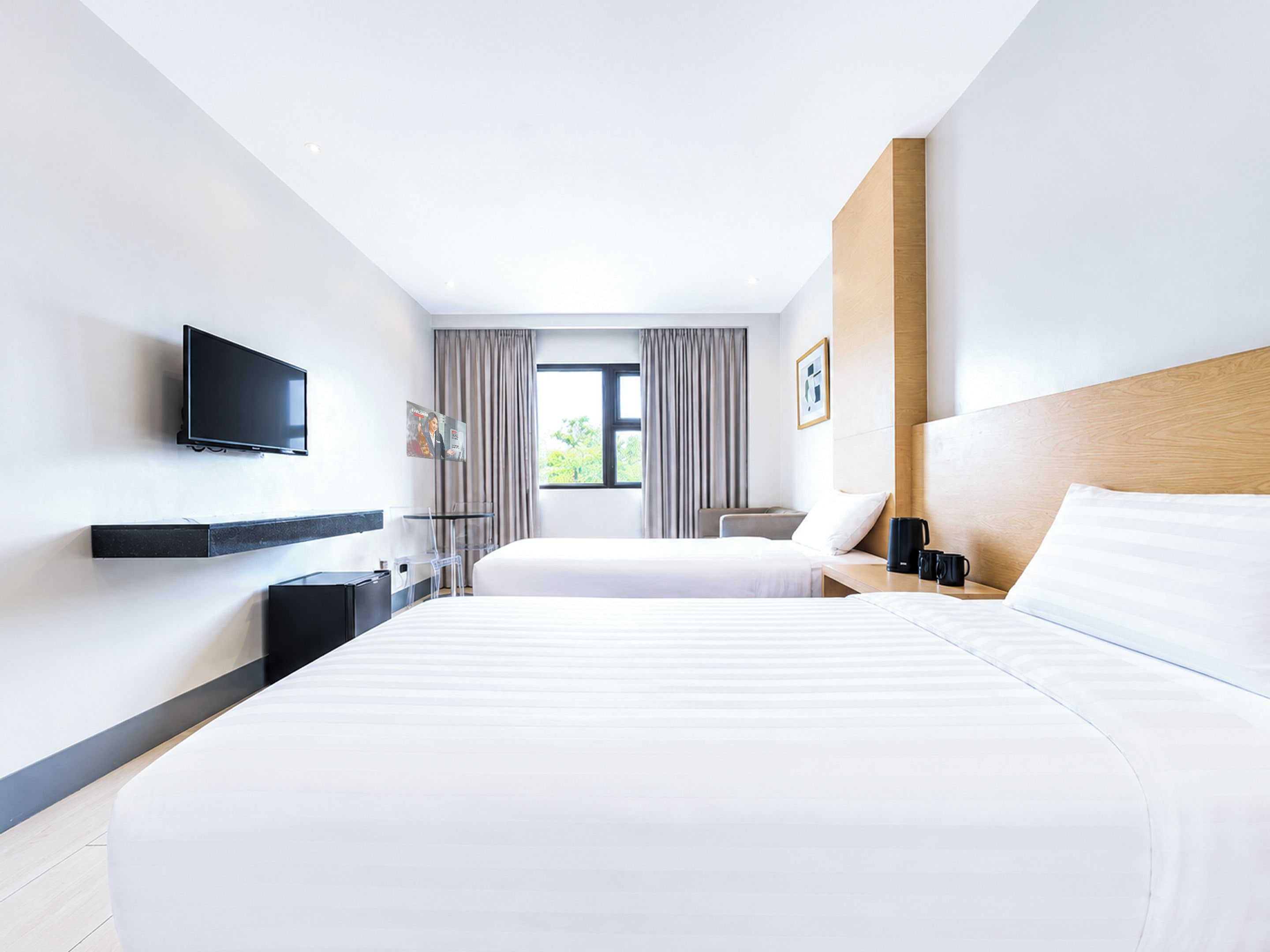 Habitación de hotel con dos camas, televisión, escritorio y ventana con cortinas.