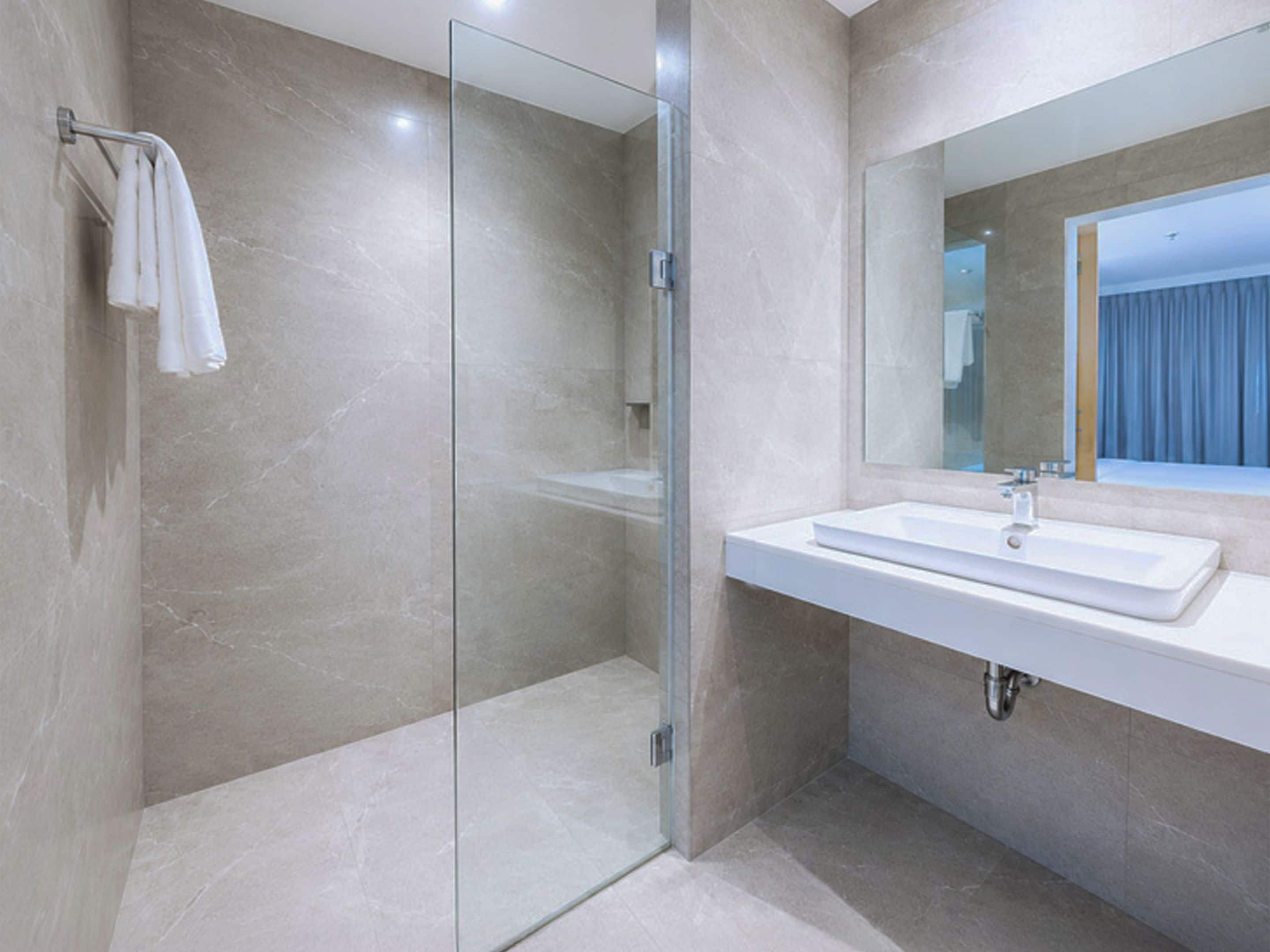 Un baño moderno con cabina de ducha de vidrio, un lavabo blanco y un espejo grande.