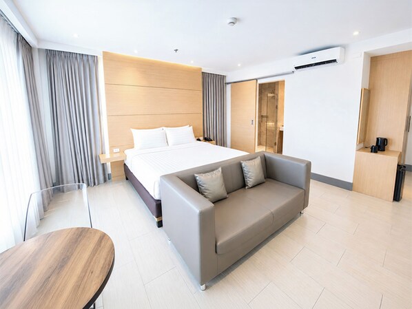 Una habitación de hotel moderna con una cama grande, un sofá, una mesa de madera y un baño visible a través de una puerta de cristal.