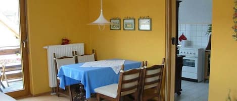 A dining area with a table set for two, a radiator, and a kitchen visible through an open doorway.