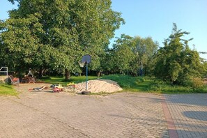 Une zone pavée avec un panier de basketball, un tas de sable et une voiture jouet.