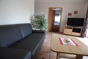 A living room with a sofa, a television on a stand, a small table with a placemat, and a potted plant. - Holiday apartment with 1 bedroom (Elbinsel Krautsand)