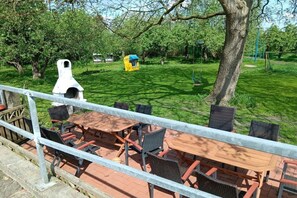 An outdoor seating area with tables and chairs, a barbecue grill, and a yellow play structure in a park. - Holiday apartment with 1 bedroom (Elbinsel Krautsand)