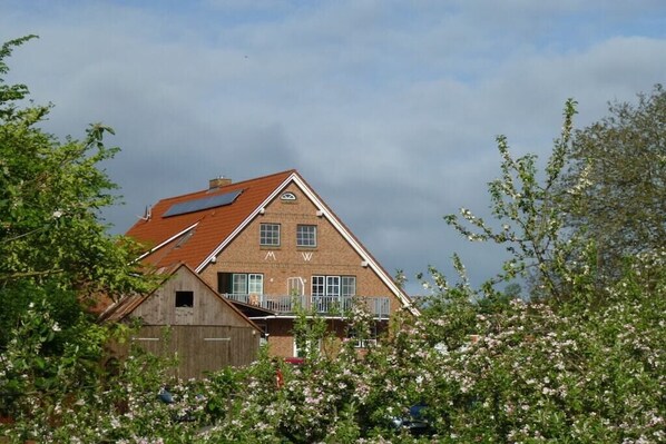 A two-story brick house with a sloped roof, a visible attic, and a small attached wooden structure. - Holiday apartment with 1 bedroom (Elbinsel Krautsand)