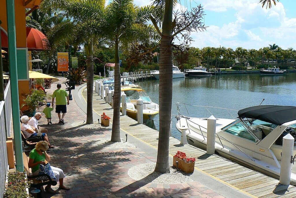 A waterfront promenade with benches, palm trees, and docked boats.