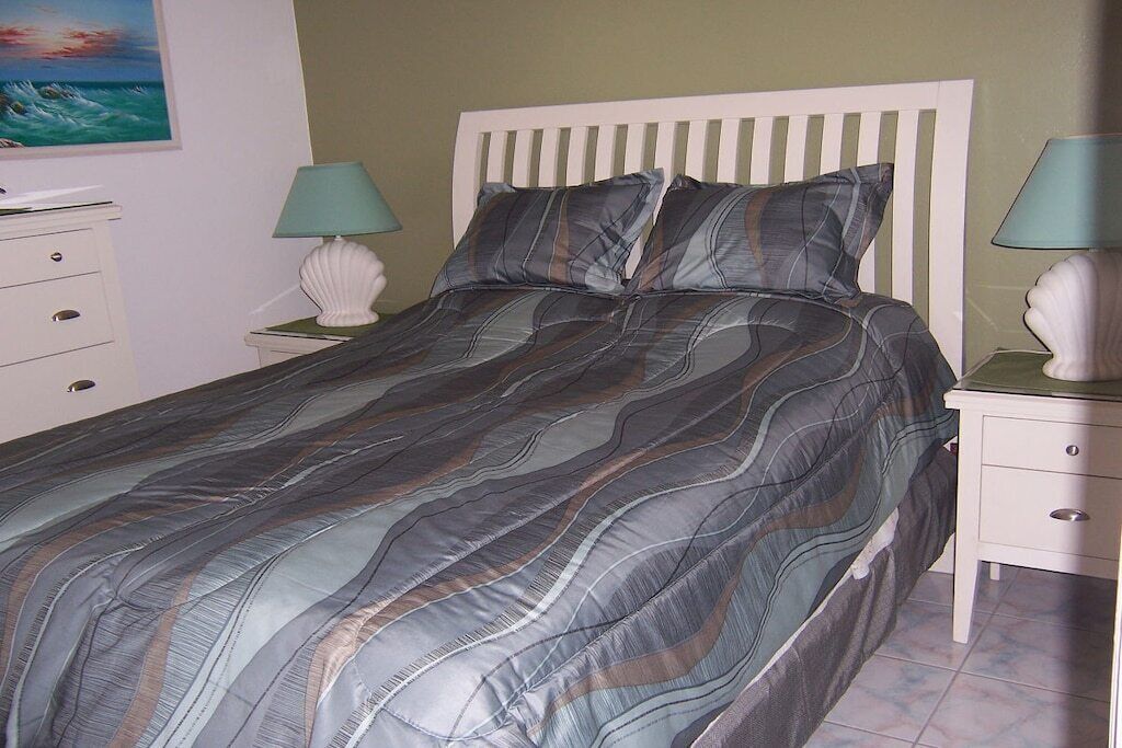 A bed with a striped bedspread, two bedside tables with lamps, a white headboard, and a painting on the wall.