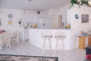A kitchen with white cabinets, a refrigerator, and a sink. There are two white bar stools and a dining table with chairs. - Villa in Cape Coral with swimming pool (Cape Coral)