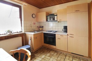 Eine kleine Küche mit Holzschränken, einem Herd, einer Mikrowelle und einem Spülbecken.