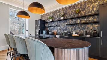 A modern kitchen with a central island, bar stools, pendant lighting, and a backsplash with a marbled pattern.