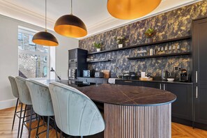 Una cocina moderna con una isla central, taburetes de bar, iluminación colgante y un salpicadero con diseño de mármol.