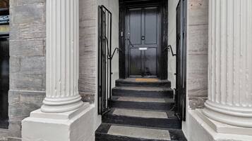 A staircase leading to a black door with a number plate, flanked by white columns and a stone wall.
