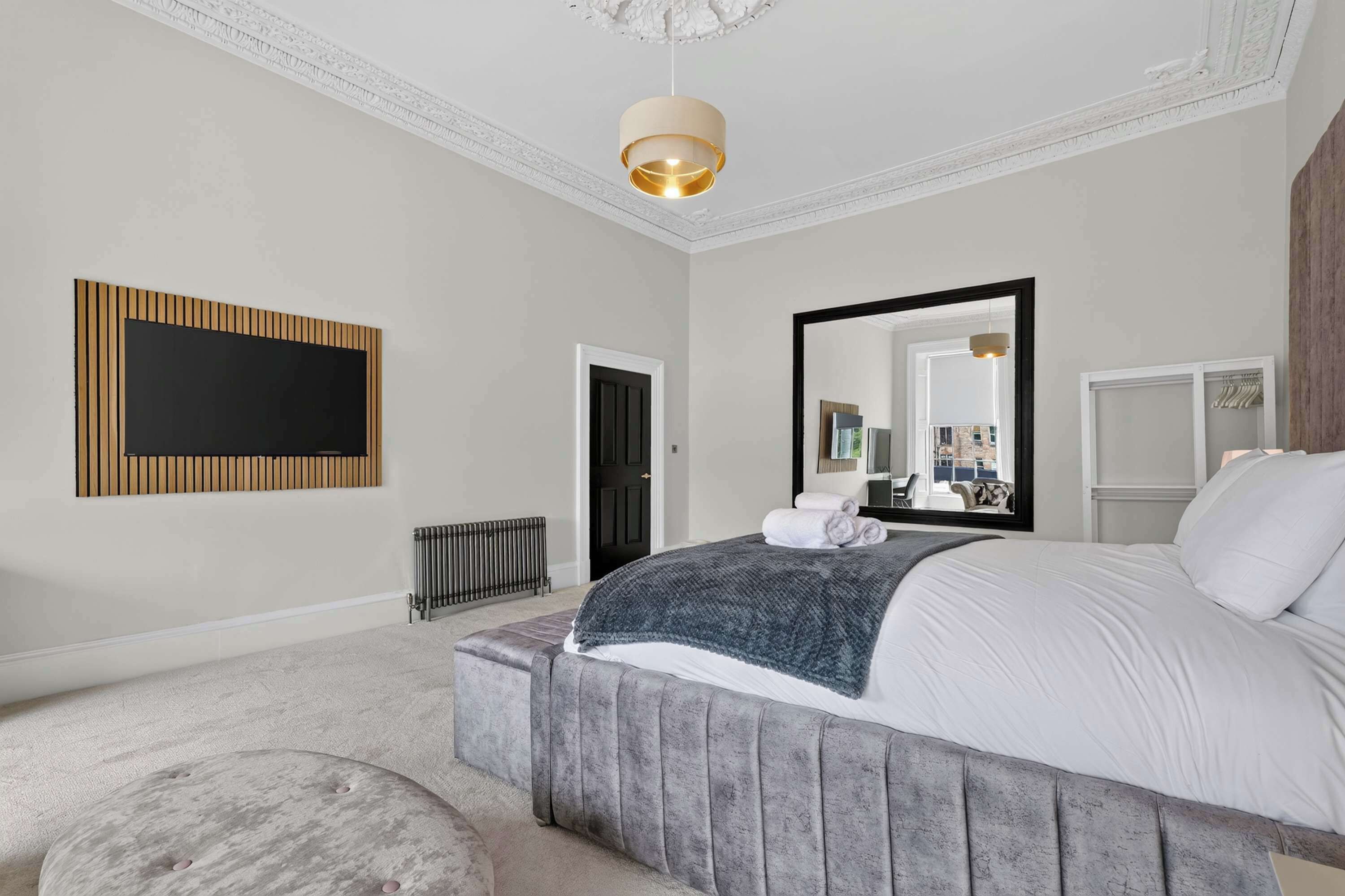 A bedroom with a large bed, a mirror, a radiator, and a wall-mounted TV.