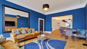 Uma sala de estar moderna com parede azul, um sofá, uma mesa de centro e um espaço de jantar com mesa e cadeiras.