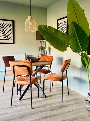 A dining area with a round table, four chairs, a hanging light fixture, and large green leaves. - Bright and Central Paisley Flat Fast Airport and Glasgow Links (Renfrewshire)