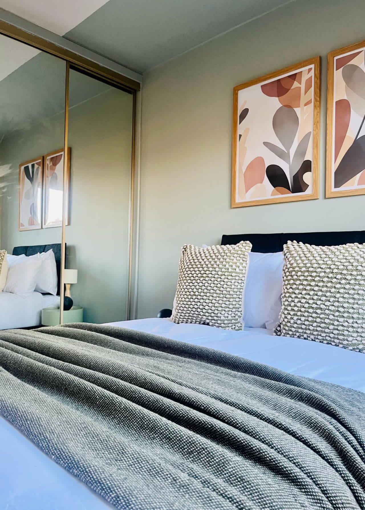 A neatly made bed with a grey textured blanket, a dark headboard, and two patterned pillows.