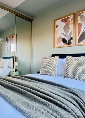 A neatly made bed with a grey textured blanket, a dark headboard, and two patterned pillows. - Bright and Central Paisley Flat Fast Airport and Glasgow Links (Renfrewshire)