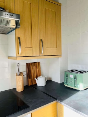 A kitchen with wooden cabinets, a black countertop, a toaster, a kettle, and a knife holder. - Bright and Central Paisley Flat Fast Airport and Glasgow Links (Renfrewshire)