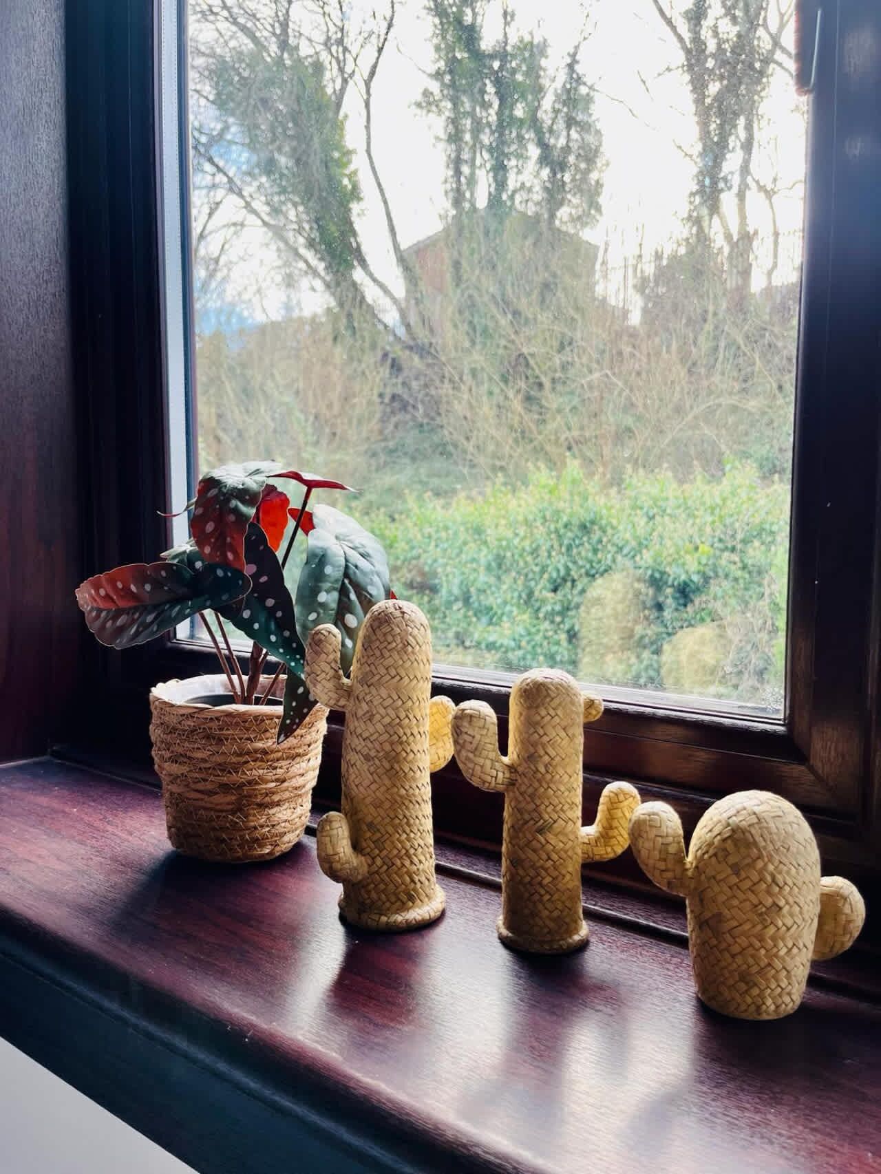 Ein Fensterbrett mit einem gewebten Korb, einer Kakteefigur und einem kaktusförmigen Gefäß.