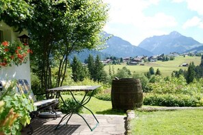 A patio with a table and chairs, a barrel, and a view of a village and mountains. - "Fellhorn" in the Schneider house (Riezlern)
